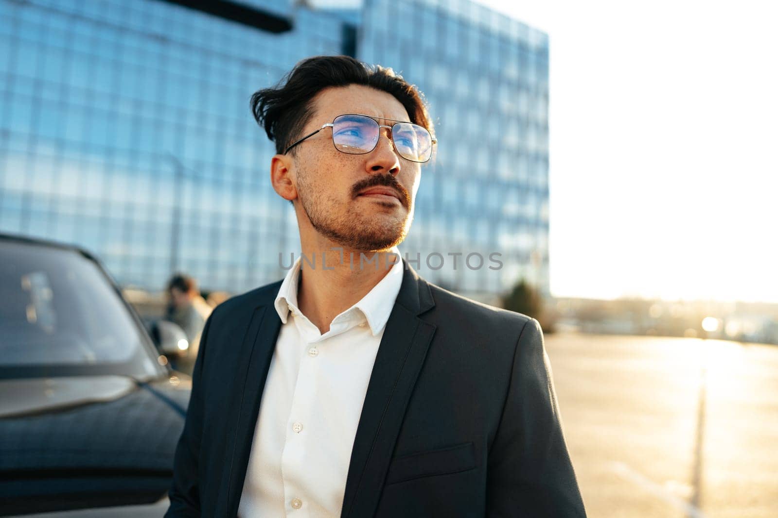 Confident young businessman in suit standing near his car outdoors