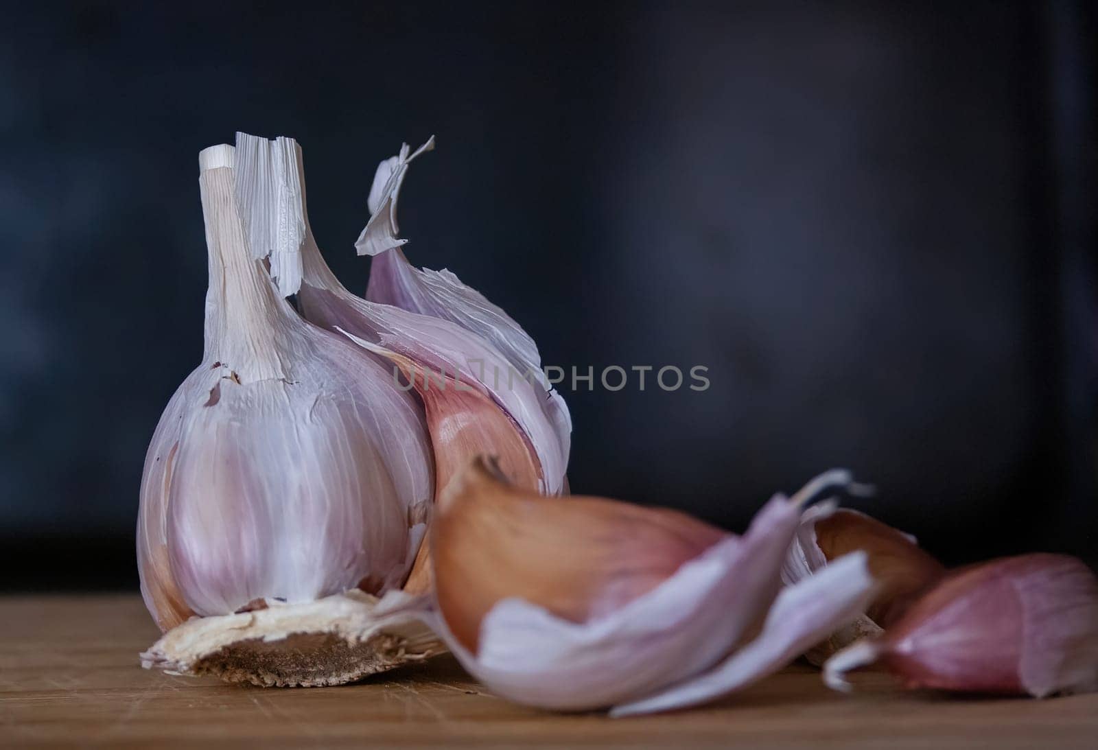 Garlic head and cloves on a wooden board with black background by VeroDibe