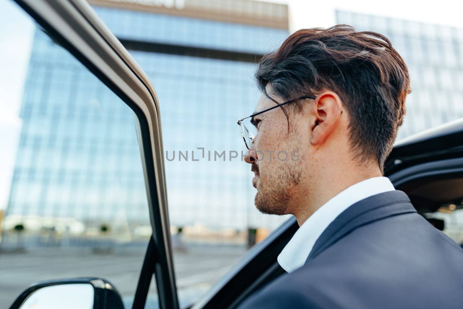 Young handsome businessman in a suit comes out of the luxury car close up