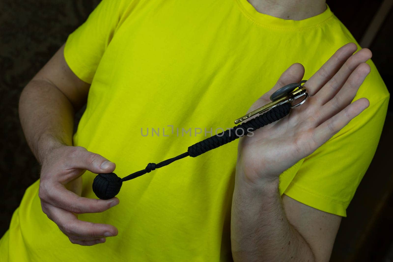 Convenient keychain made of paracord hangs on keys for self-defense, metal ball acting as baton is covered with laces