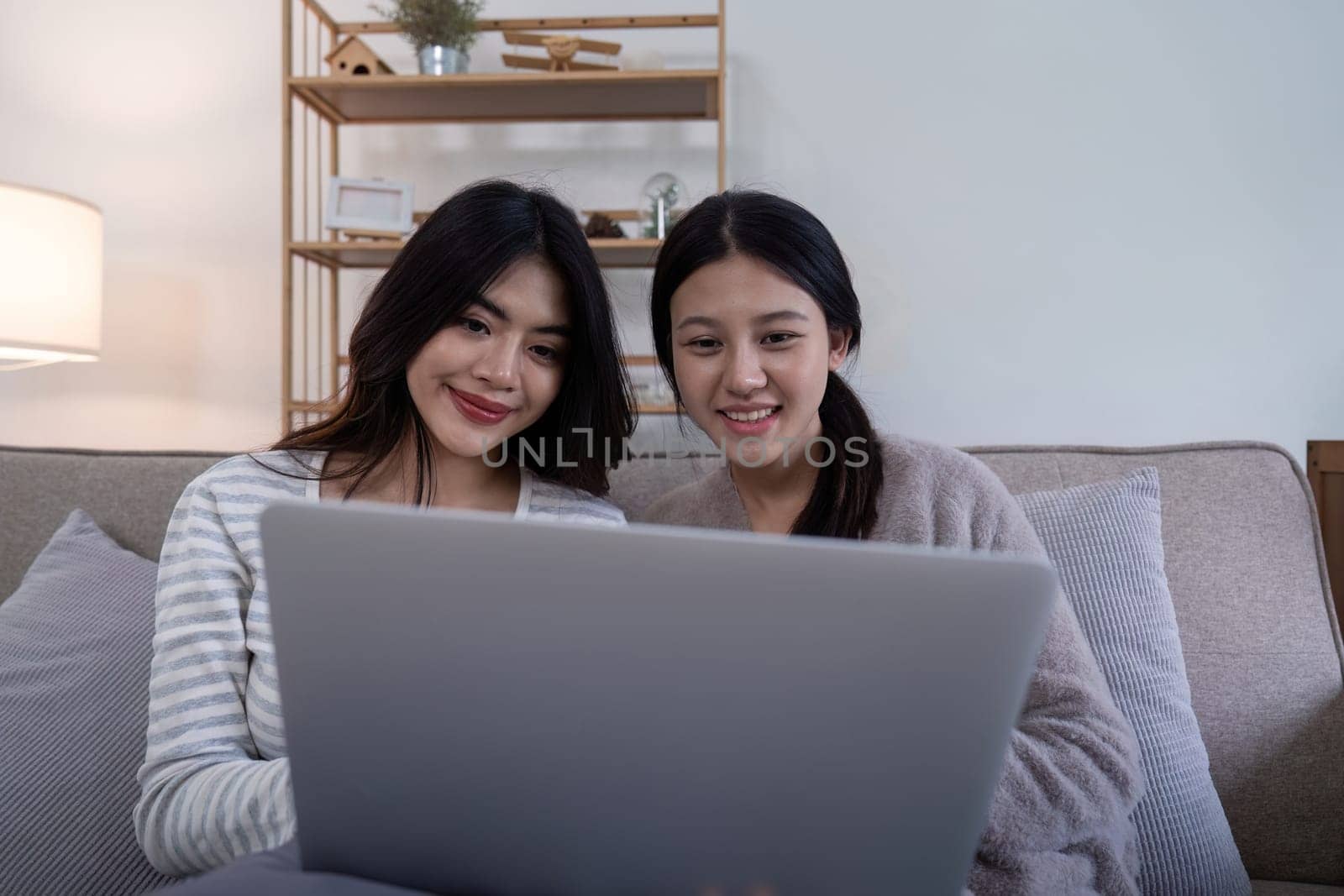 Asian lesbian couple using laptop together at home. Concept of technology and companionship.