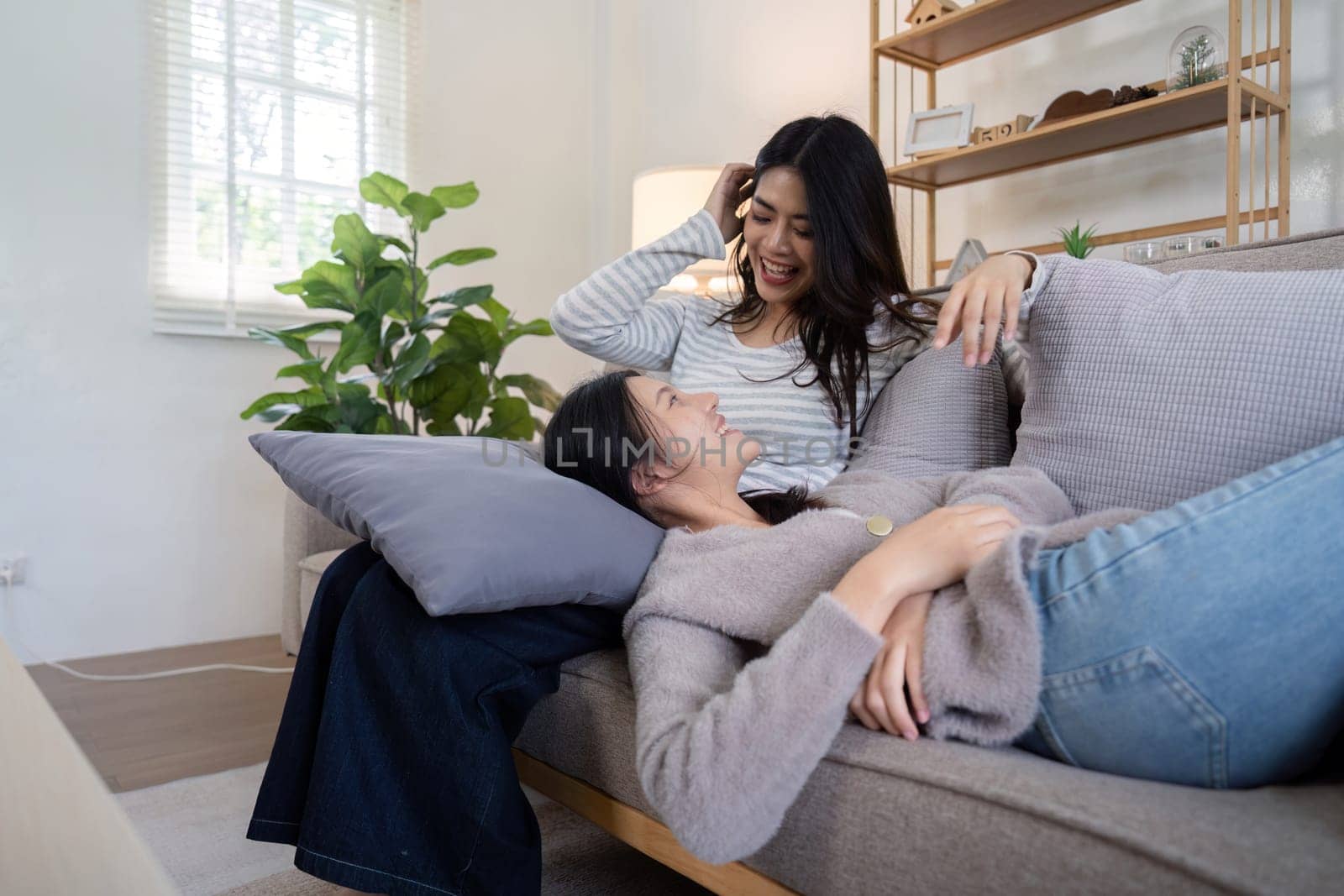 Asian lesbian couple relaxing on sofa at home. Concept of love and companionship.