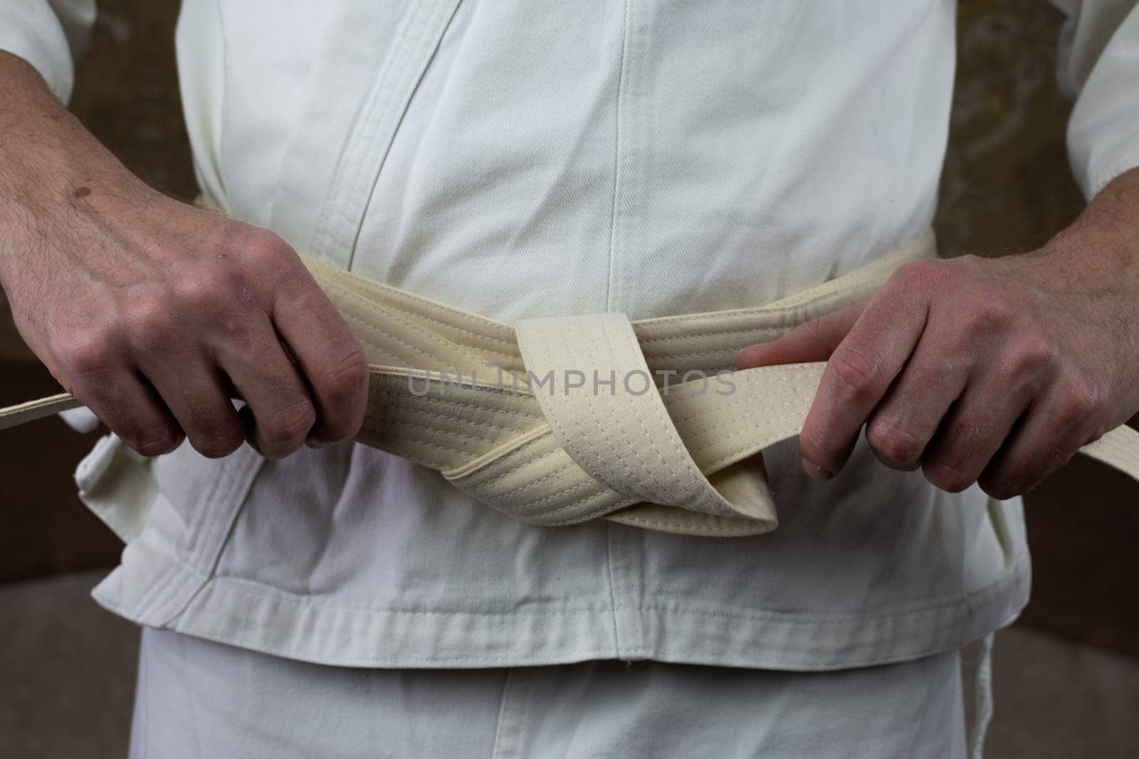 Kyokushin karate athlete tightens a white belt on kimono before a competition, preparing karate equipment