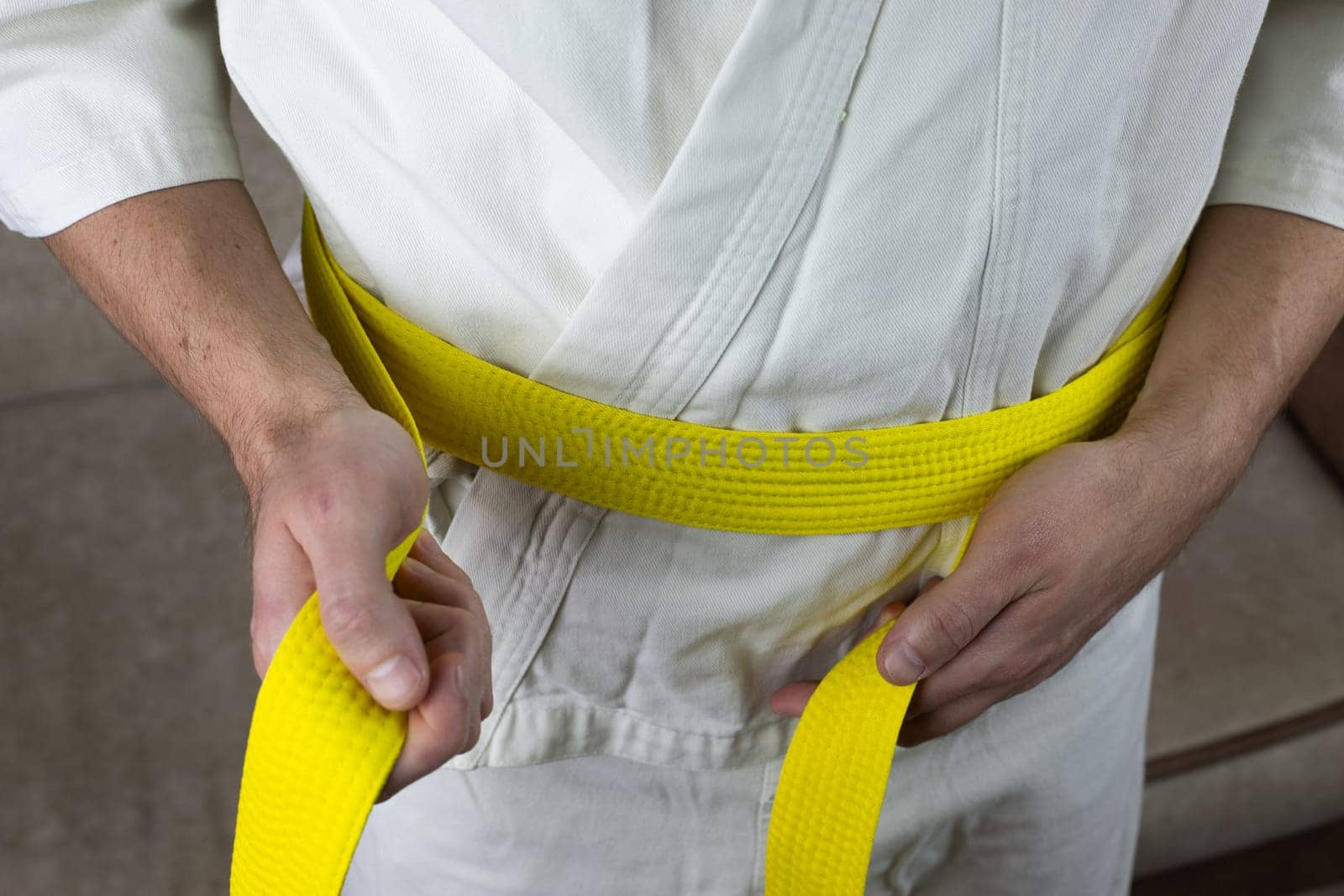 Man ties yellow Kyokushin karate belt on kimono around his waist by timurmalazoniia