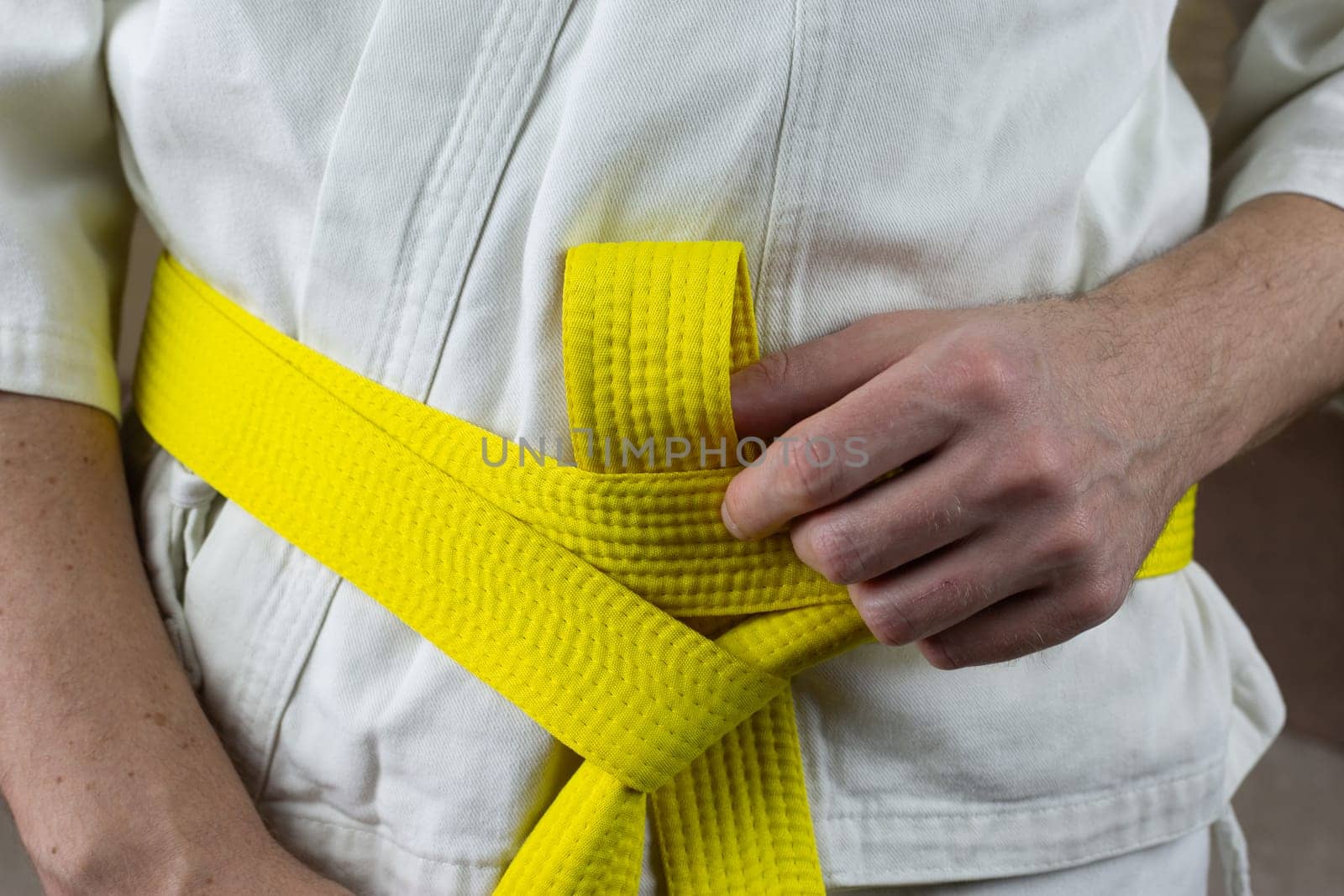 Male hands tighten yellow karate belt on kimono by timurmalazoniia