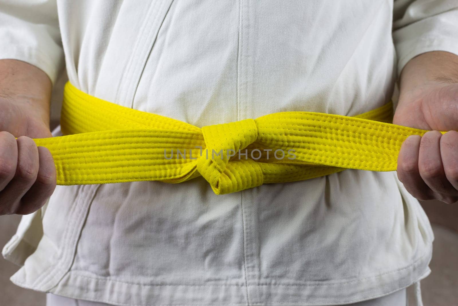 Male hands tighten yellow belt in Kyokushin karate, Asian types of martial arts with belts, the sixth kyu puts belt on karate kimono