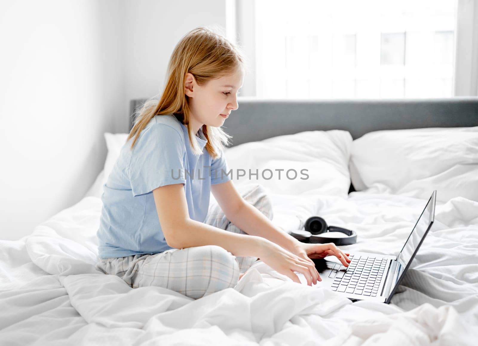 Girl Sits In Bed With Laptop In Bright Room In The Morning