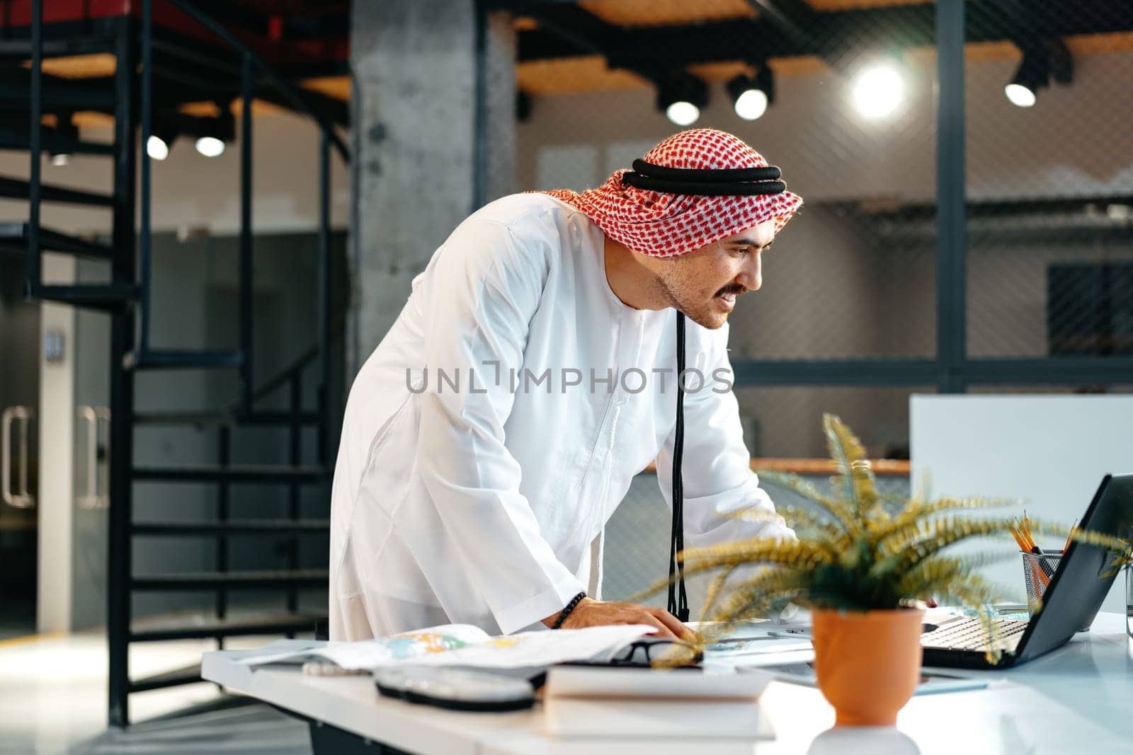 Young muslim businessman in traditional outfit working at the table in office clsoe up