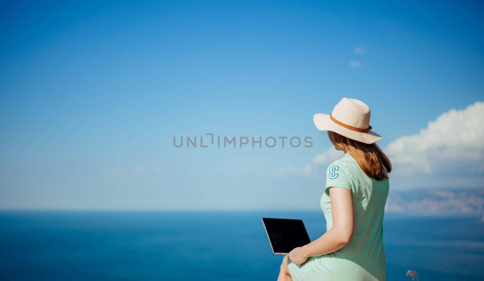 A woman is sitting on a rock by the ocean with a laptop in front of her by Matiunina