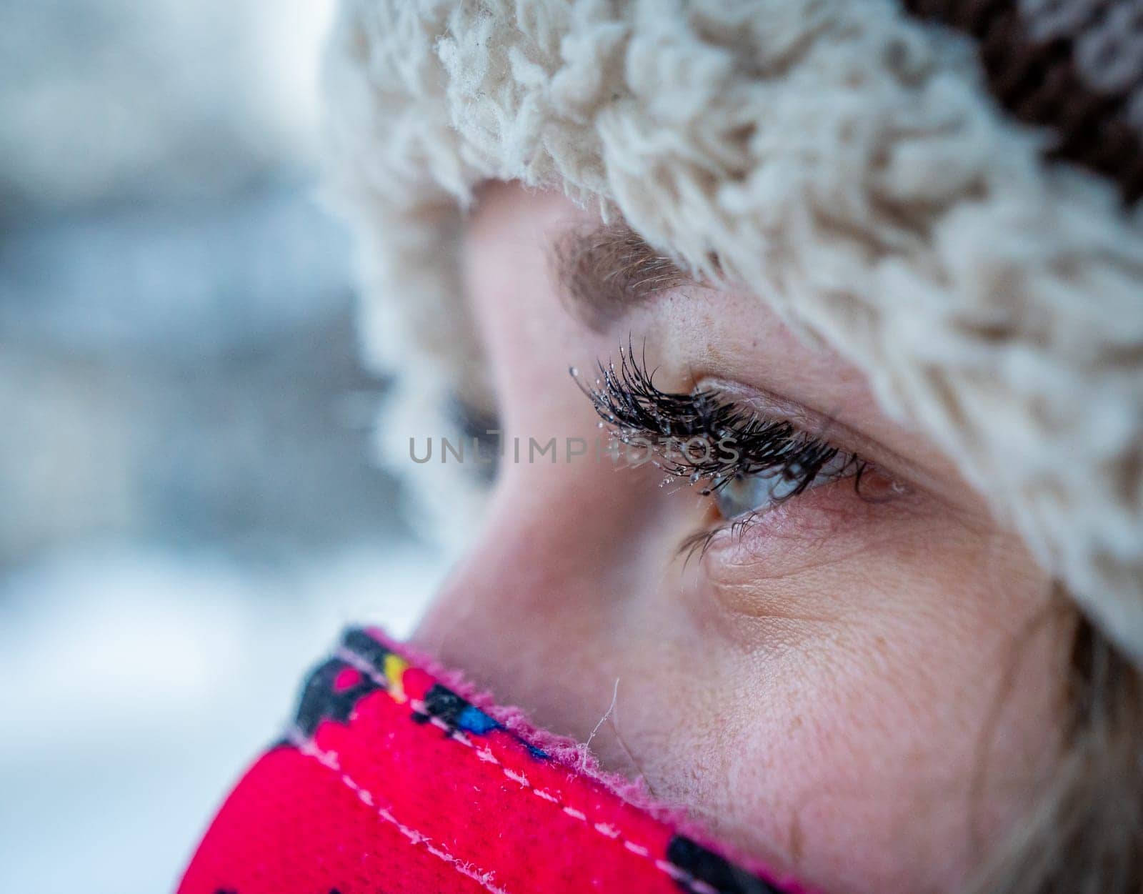 Young woman with blue eyes wearing a winter hat and scarf in snowy weather by Busker