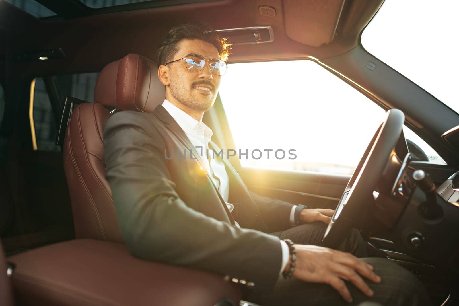 Young businessman in elegant suit driving luxury car close up