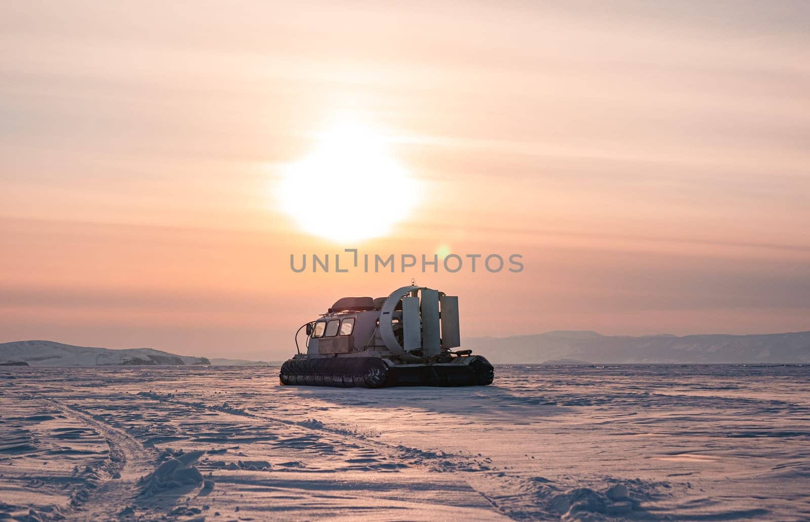 Hovercraft standing on snow covered ice surface of Lake Baikal at dusk. by Busker