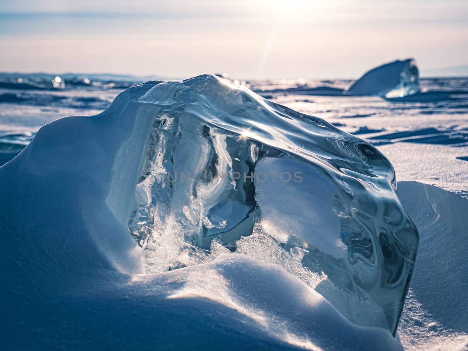A stunning block of ice sits on the snow, shimmering in the early morning light of a winter sunrise on Lake Baikal, Siberia.