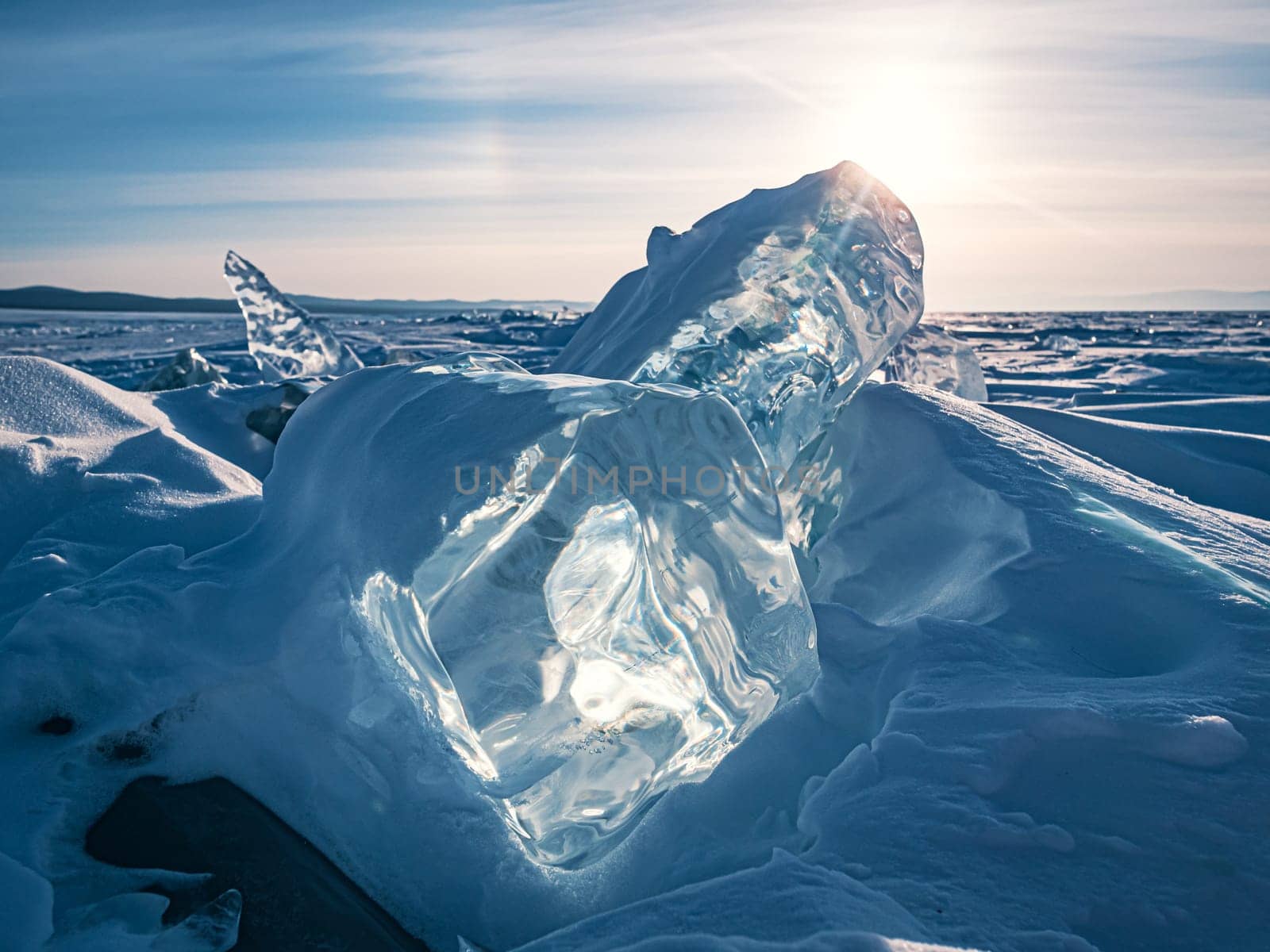 The serene landscape of Lake Baikal in winter, featuring captivating, transparent ice formations under a bright sky with the sun shining brightly above.