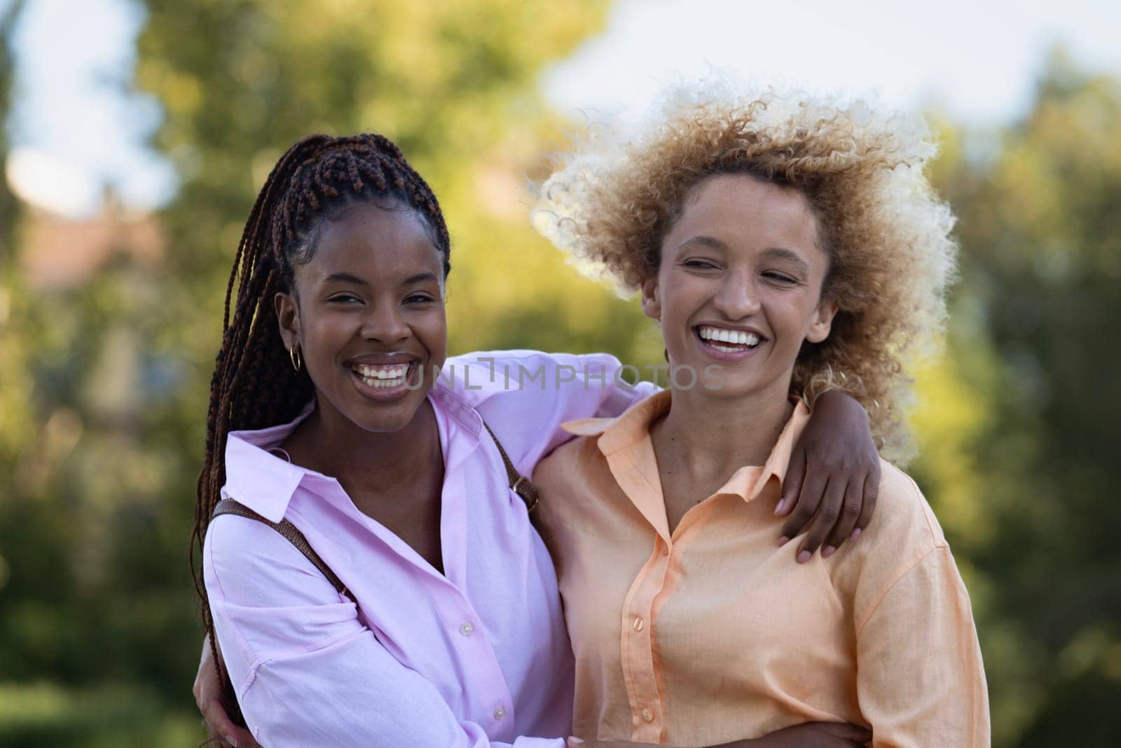 Two multiethnic women friends smiling and hugging each other in a park.