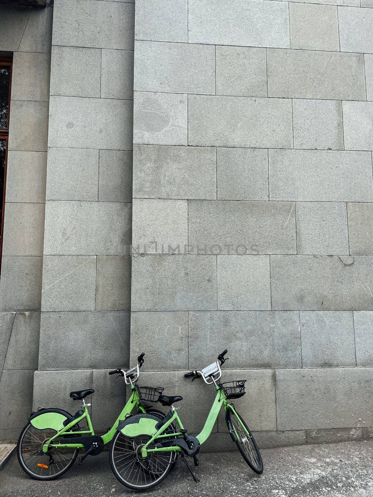 Two green bicycles for a ride around stand by the wall without people