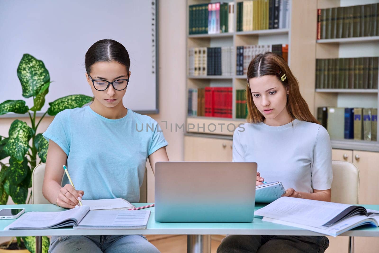 Teenage girls high school students sitting at desk in library classroom, studying together. Education adolescence communication concept