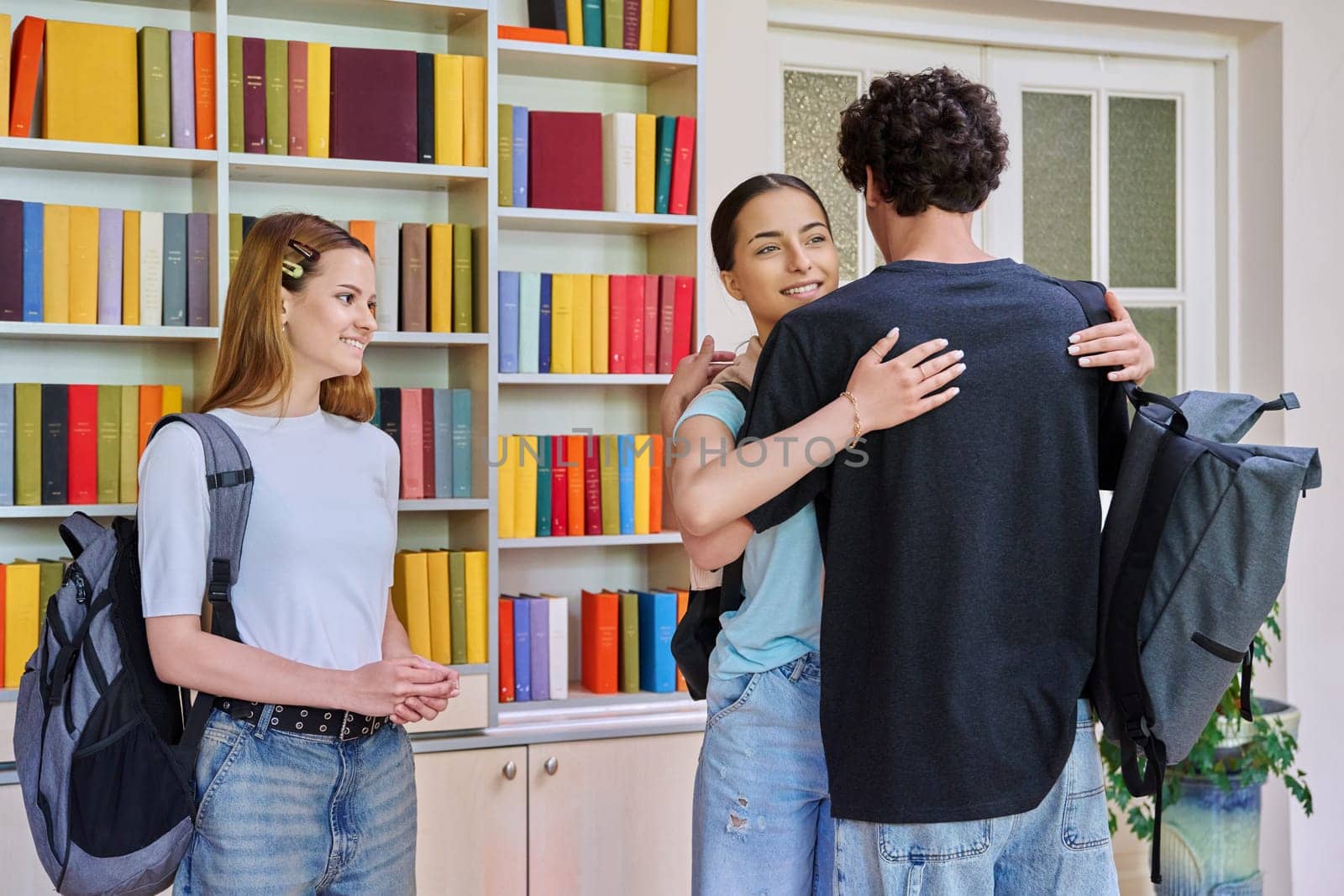 Classmates meeting in the high school library, teenagers students hugging and greeting each other. Friendship, communication, adolescence, education concept