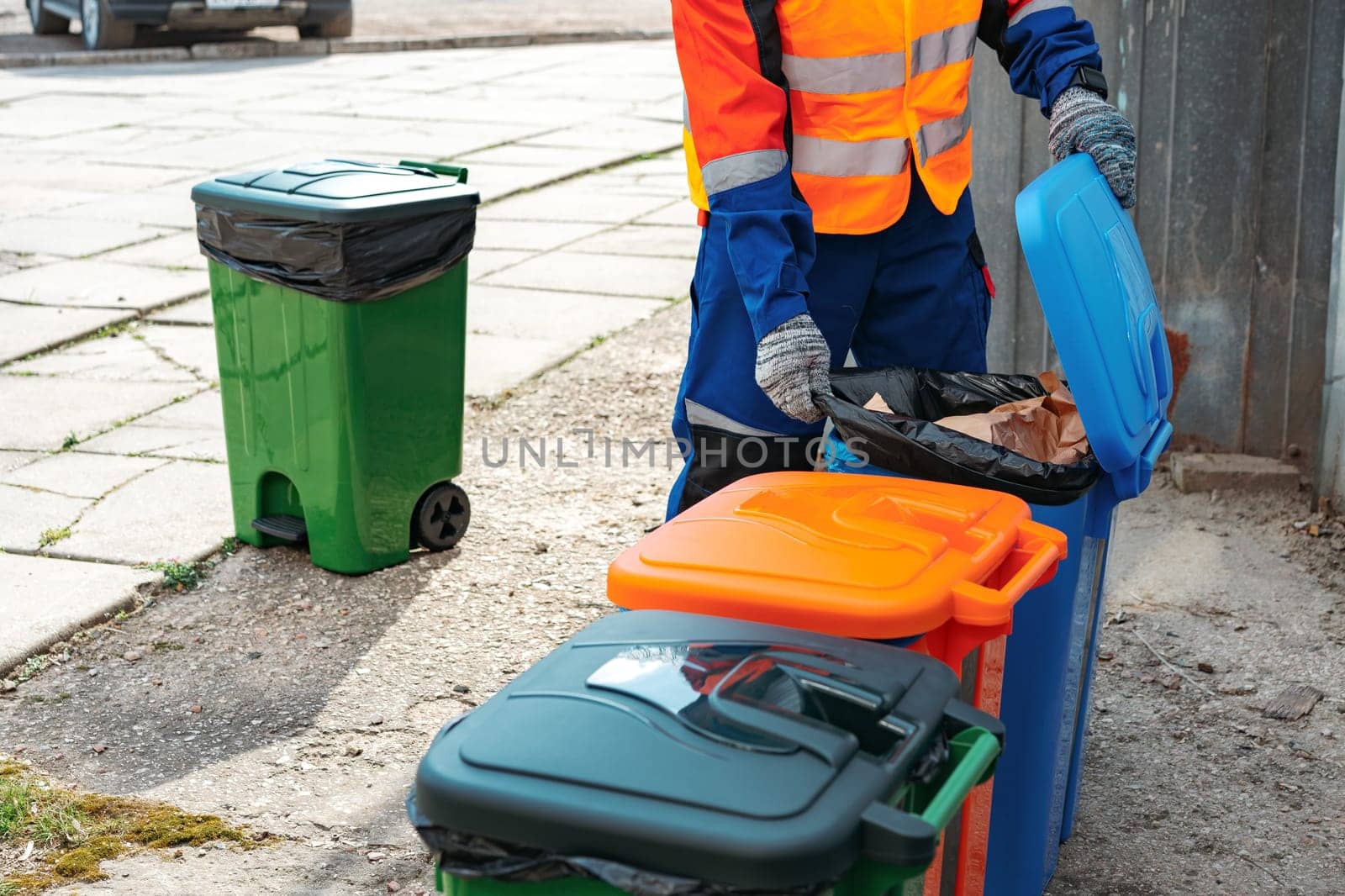 Male janitor in uniform cleans a trash can in the street close up