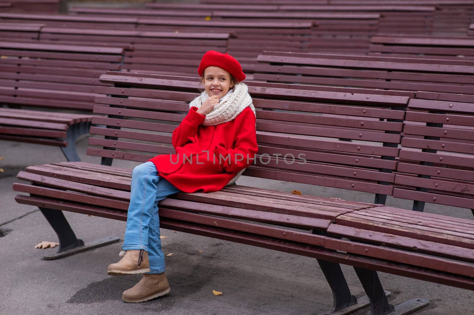 A pensive Caucasian girl in a red coat and beret sits on a bench. by mrwed54