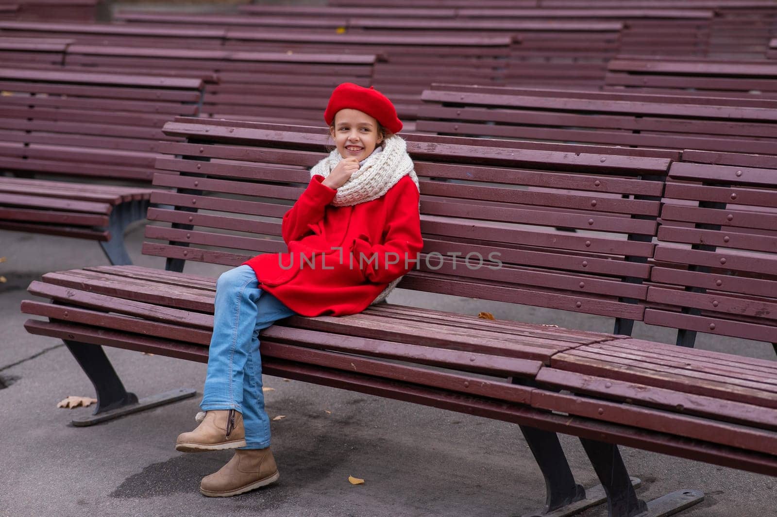 A pensive Caucasian girl in a red coat and beret sits on a bench