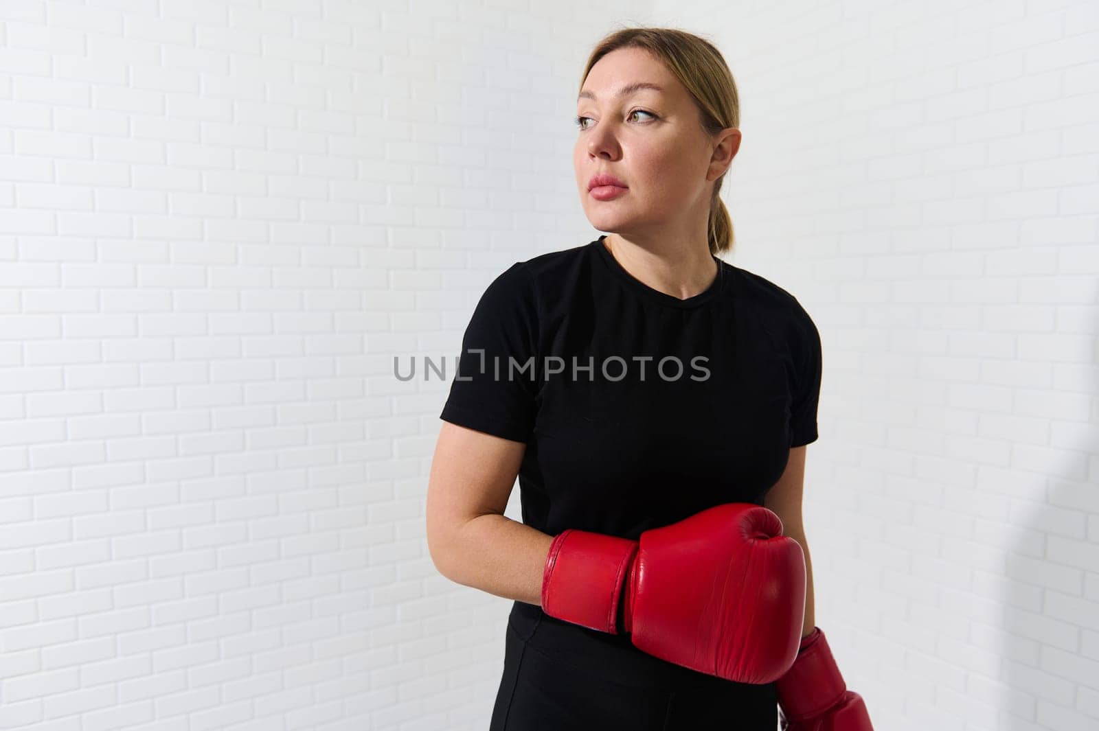 Beautiful confident European woman in sportswear and red boxing gloves, looking aside, practicing box and kickbox, isolated over white wall background. Martial art concept. Copy advertising space