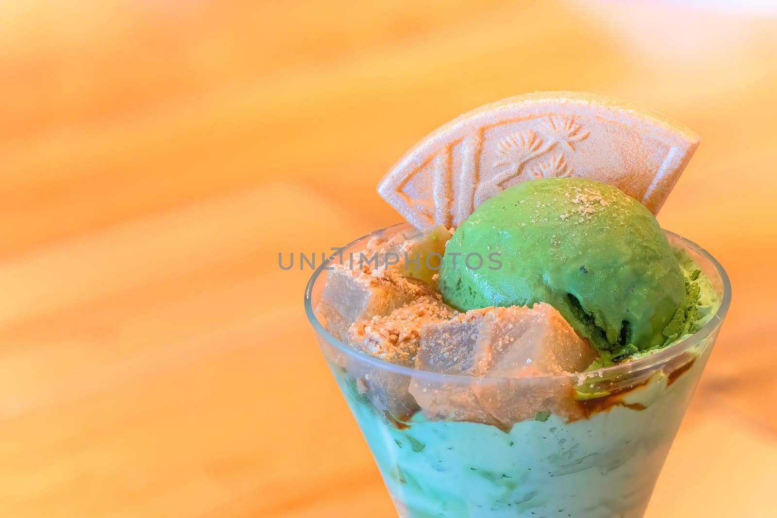 A traditional Japanese dessert matcha ice cream parfait with cubes of agar jelly sprinkled with roasted soybean flour called kinako powder and a higashi mochi wafer featuring a pine motif.