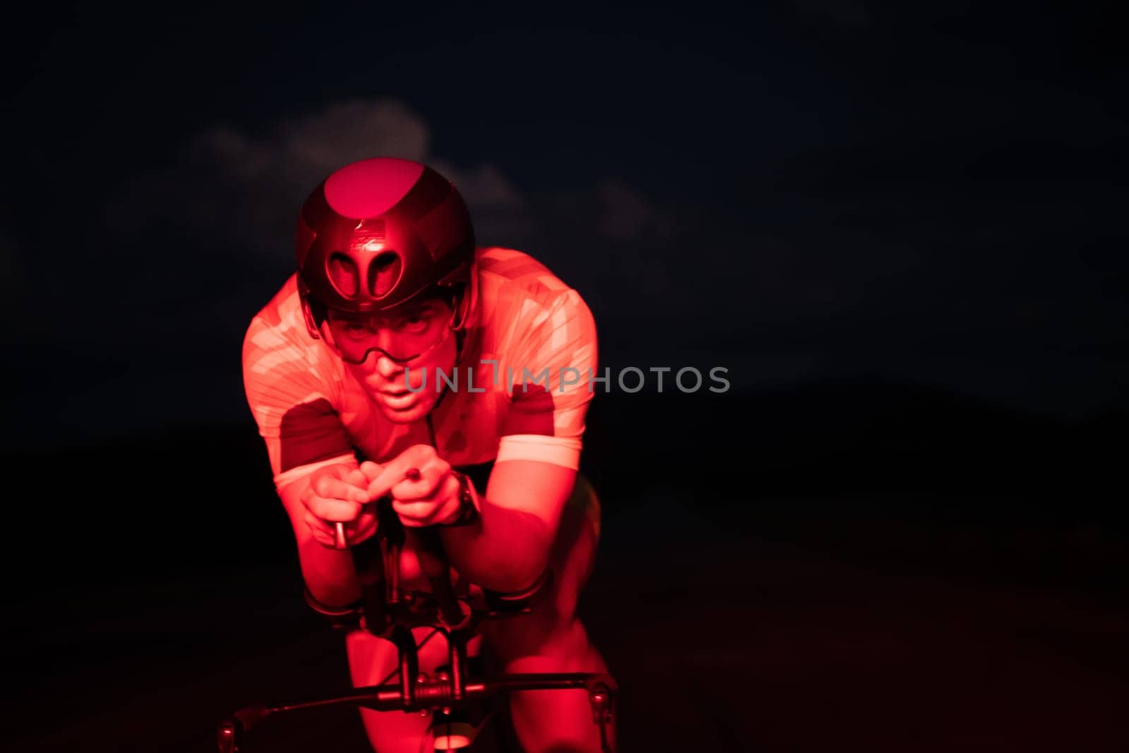 A triathlete rides his bike in the darkness of night, pushing himself to prepare for a marathon. The contrast between the darkness and the light of his bike creates a sense of drama and highlights the athlete's determination and perseverance. by dotshock