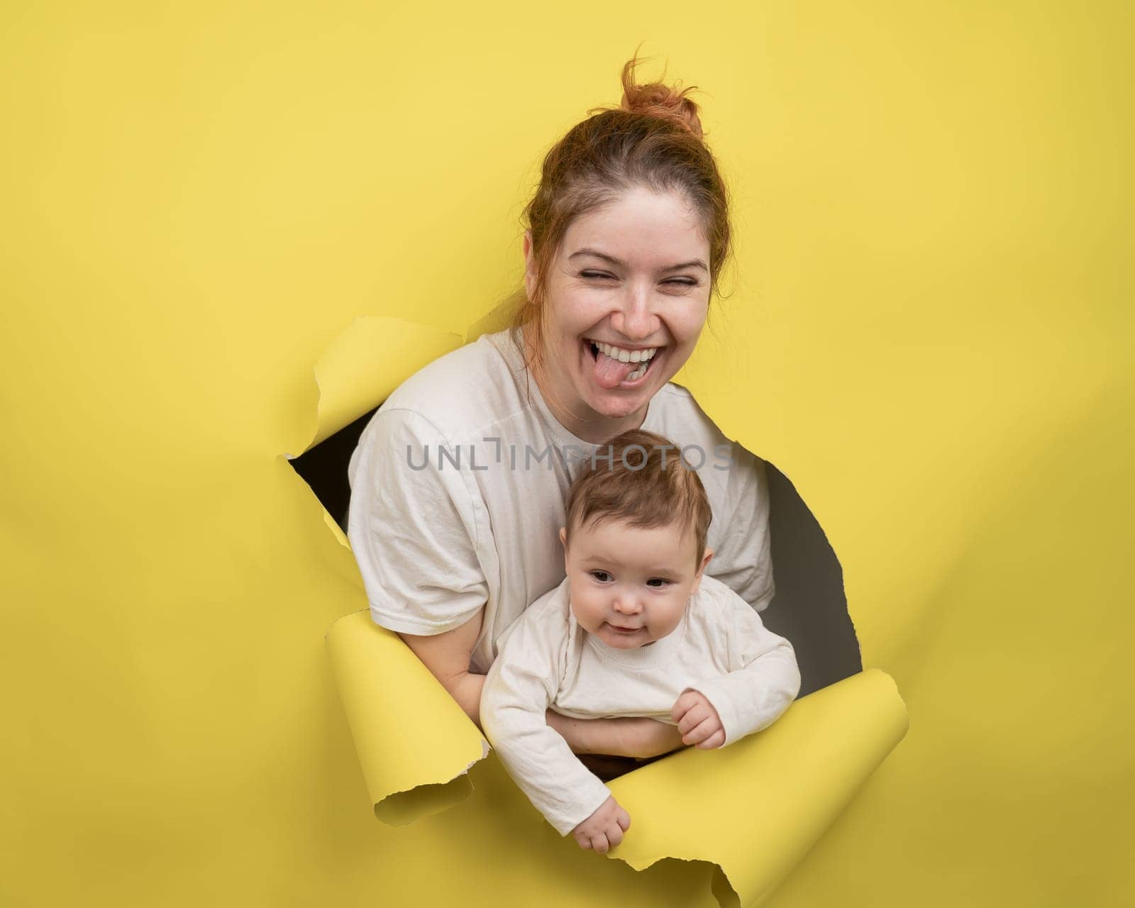 Cheerful Caucasian woman with little son rips and leans out through yellow cardboard background. by mrwed54
