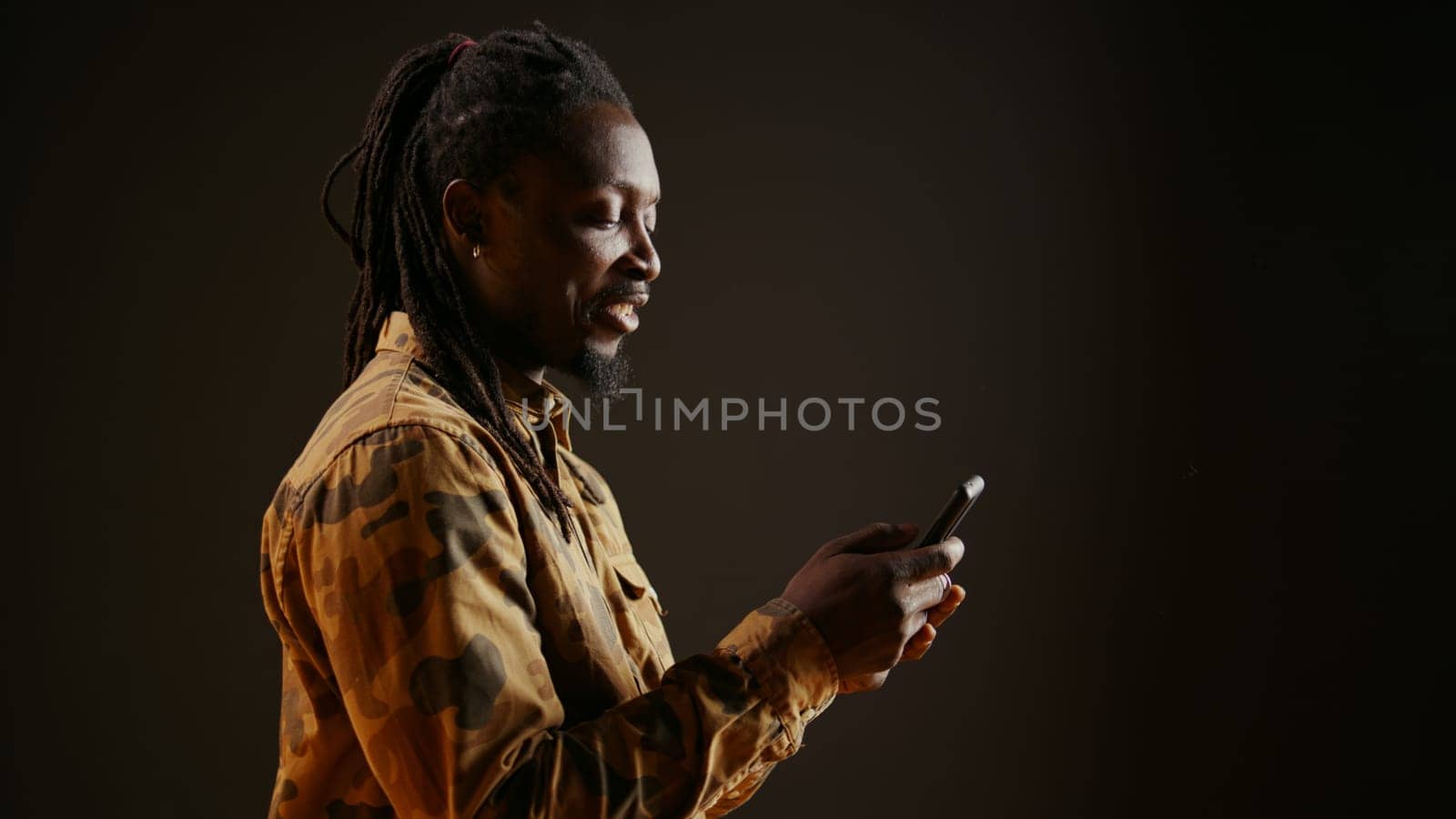 Modern person browsing online webpages on mobile phone, checking his socials for texts and posing in studio. African american man using smartphone apps to stay connected with friends.