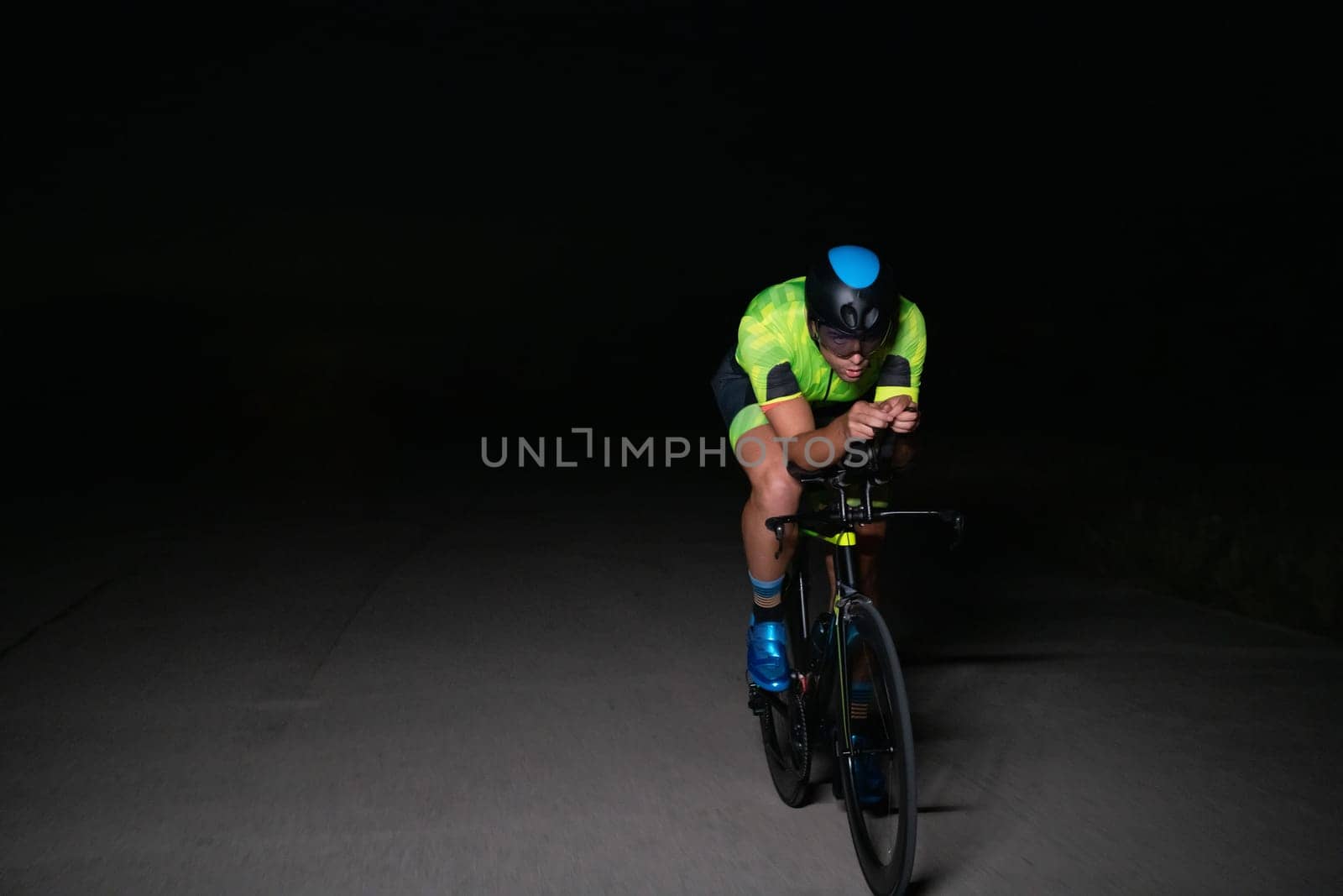 A triathlete rides his bike in the darkness of night, pushing himself to prepare for a marathon. The contrast between the darkness and the light of his bike creates a sense of drama and highlights the athlete's determination and perseverance