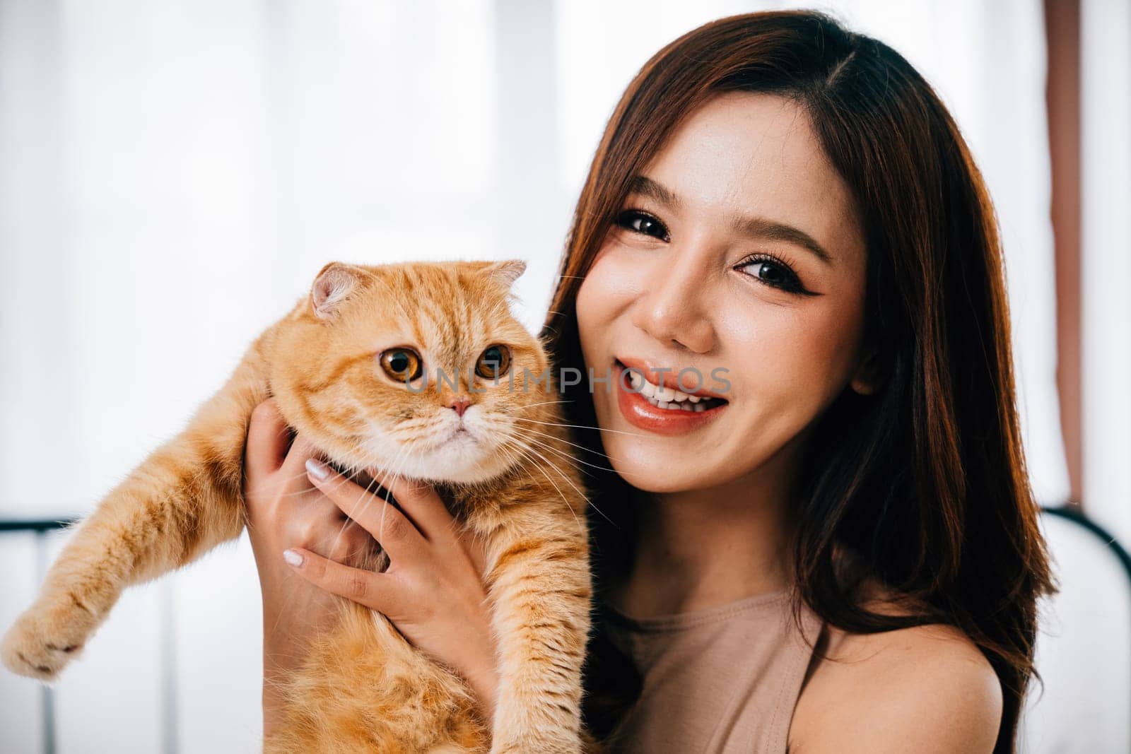A touching portrait captures a woman's affectionate embrace of her beloved orange Scottish Fold cat. The image radiates joy, love, and the special connection between them.
