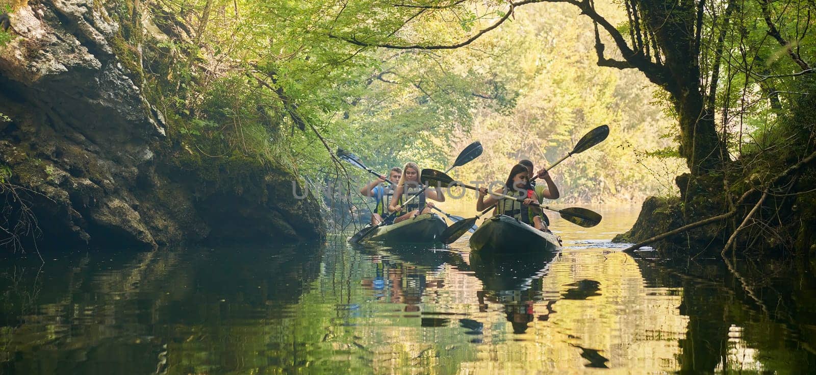 A group of friends enjoying having fun and kayaking while exploring the calm river, surrounding forest and large natural river canyons.