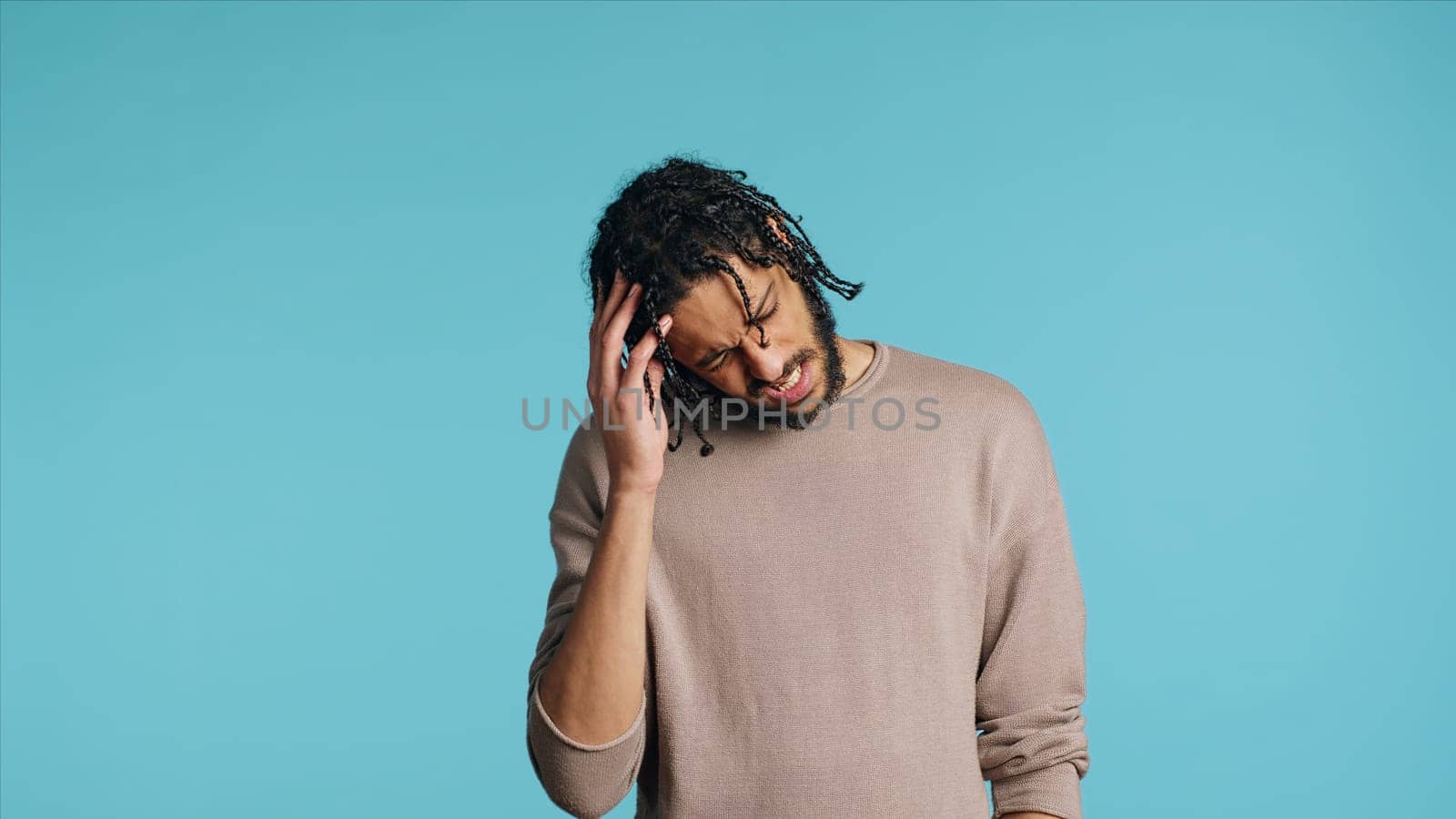 Hurt Middle Eastern man wincing from pain, suffering from headache, having health problems. Injured BIPOC person rubbing head temples, feeling discomforting strain, studio background, camera A