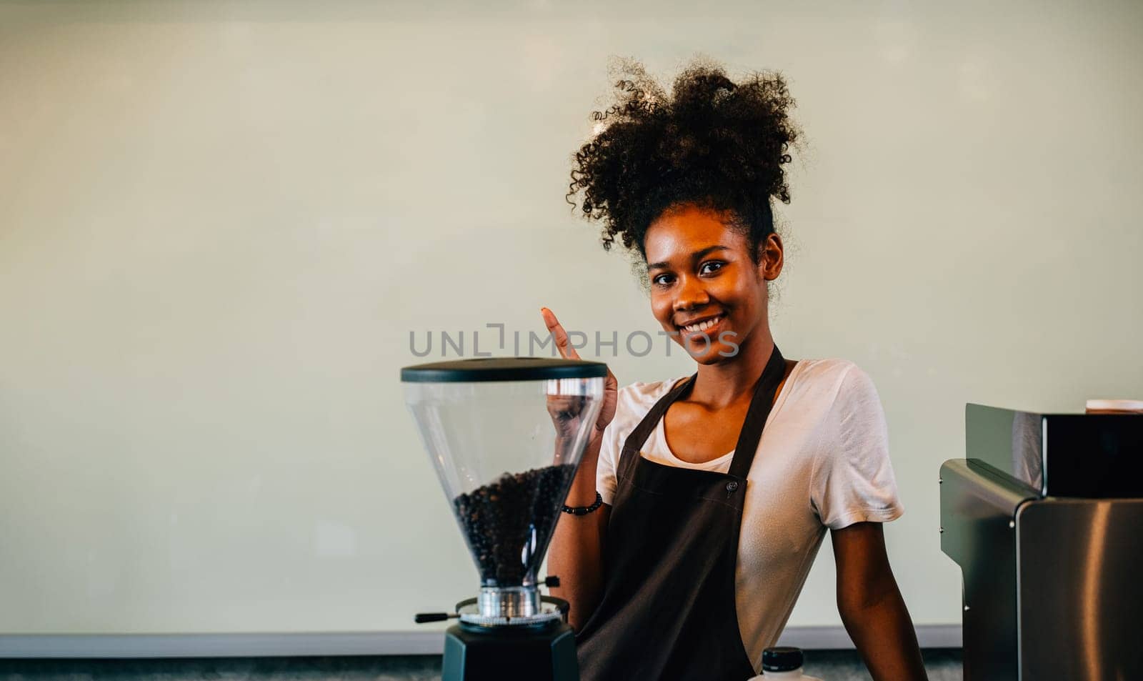 Portrait of confident black woman owner standing at coffee shop counter. Successful businesswoman in uniform smiling with satisfaction providing excellent service. Inside a small business cafe by Sorapop