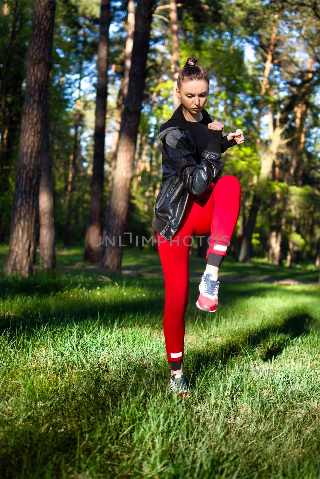 Active woman in red sportswear stretches before a run in a sunny green park
