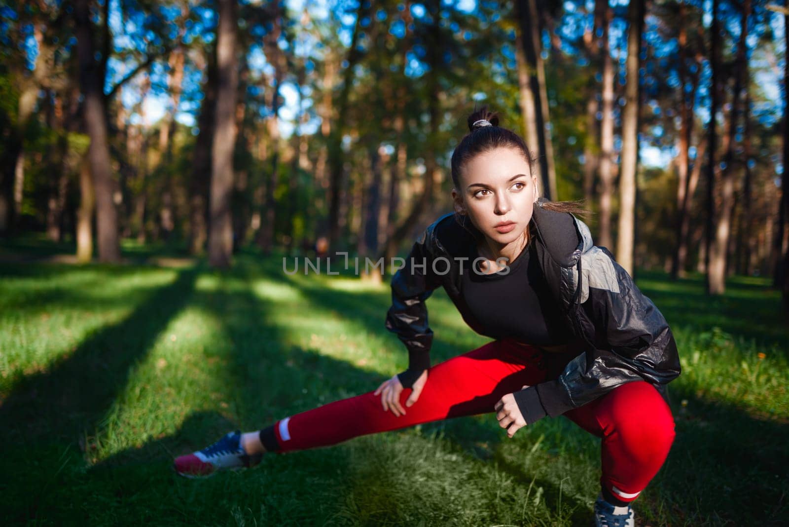 Focused young woman performs a stretch routine in a serene forest, embracing a healthy lifestyle