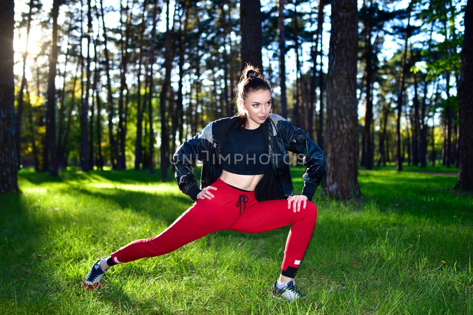 Woman in red workout pants stretching outdoors in a forest. Exercising in nature.