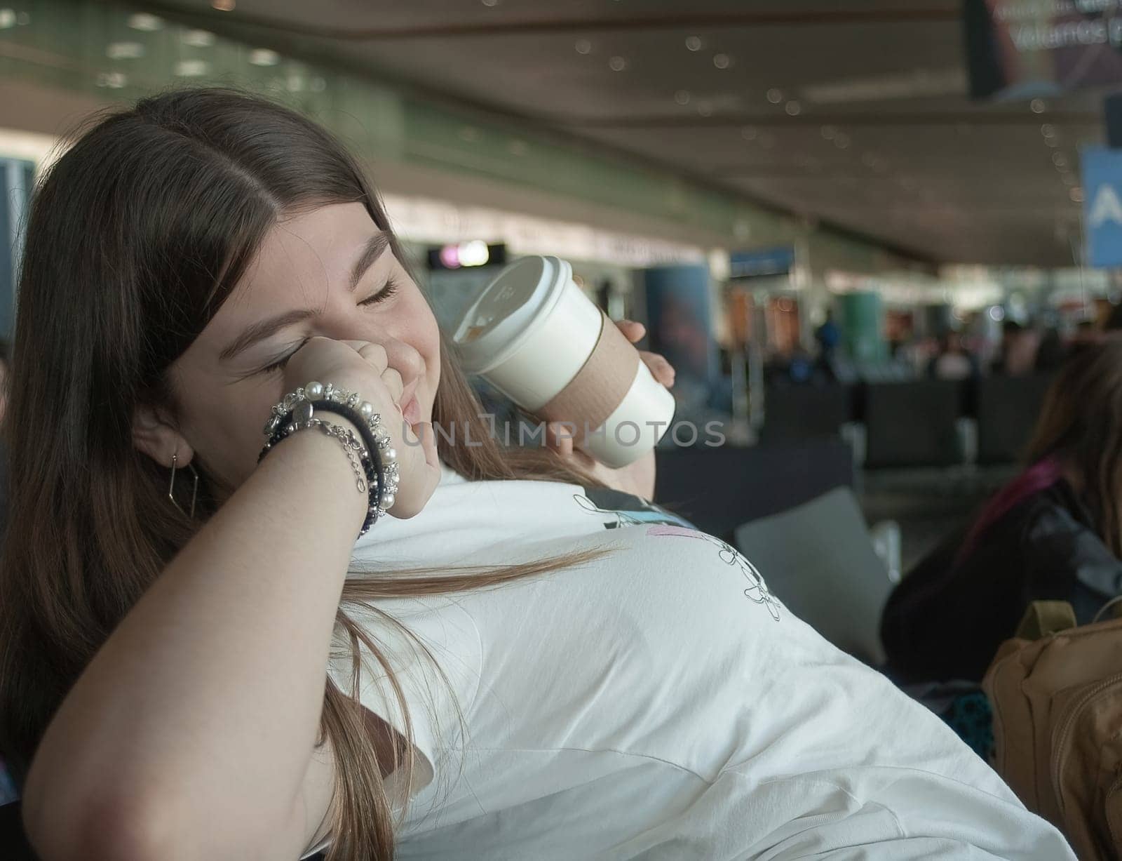 Teenager resting at the airport during a stopover with a coffe in her hand by VeroDibe