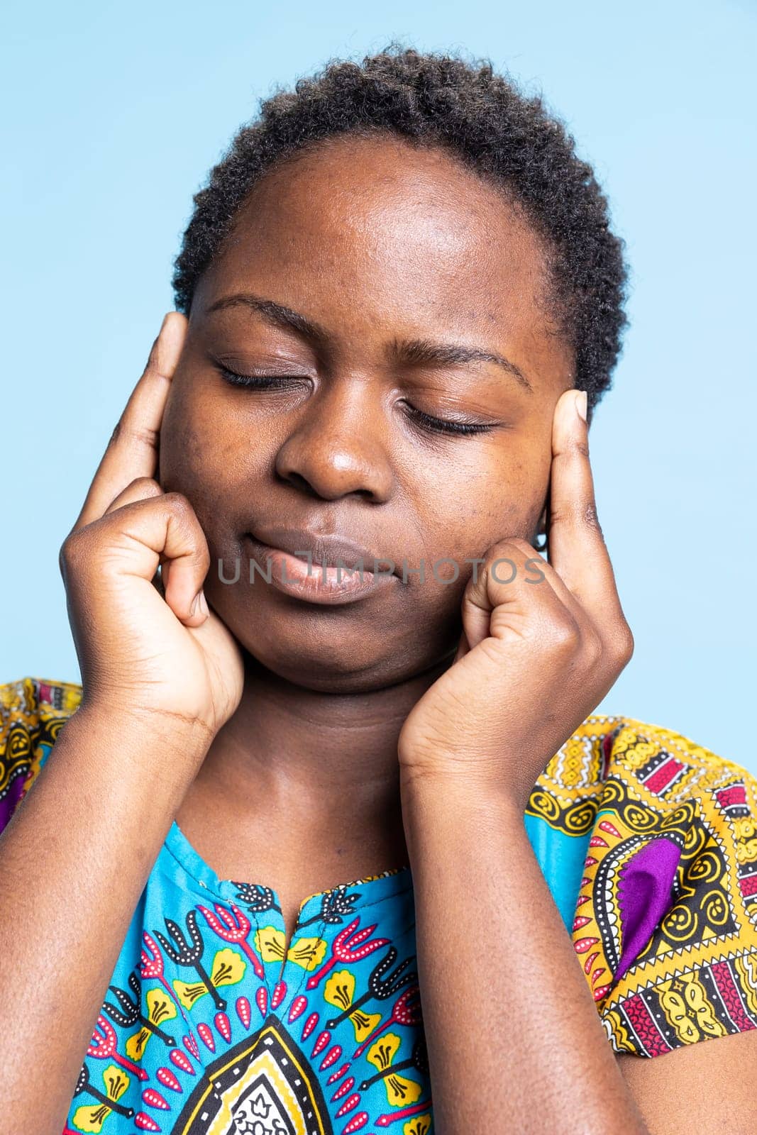 African american girl being unwell with serious migraine, experiencing flu symptoms against blue background. Sick woman in pain having medical issues, painful headache in studio.