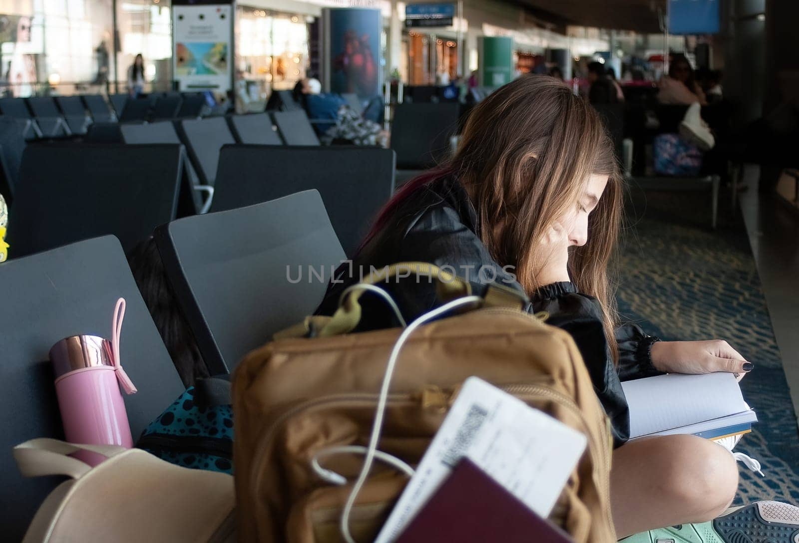 Girl with her luggage and documente, readinga book on an international airport stopover