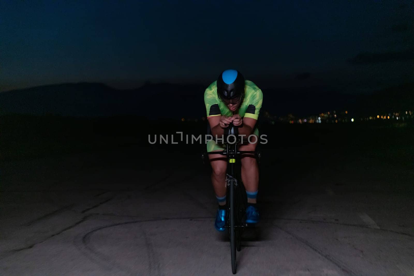 A triathlete rides his bike in the darkness of night, pushing himself to prepare for a marathon. The contrast between the darkness and the light of his bike creates a sense of drama and highlights the athlete's determination and perseverance