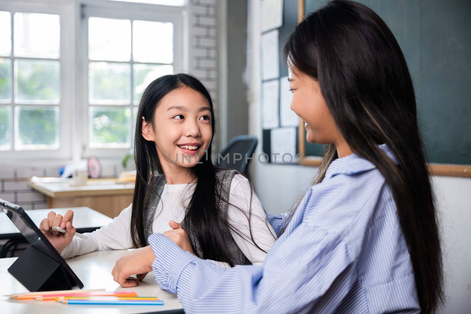 Two girls are sitting at a table, one of them is smiling and the other is looking at her