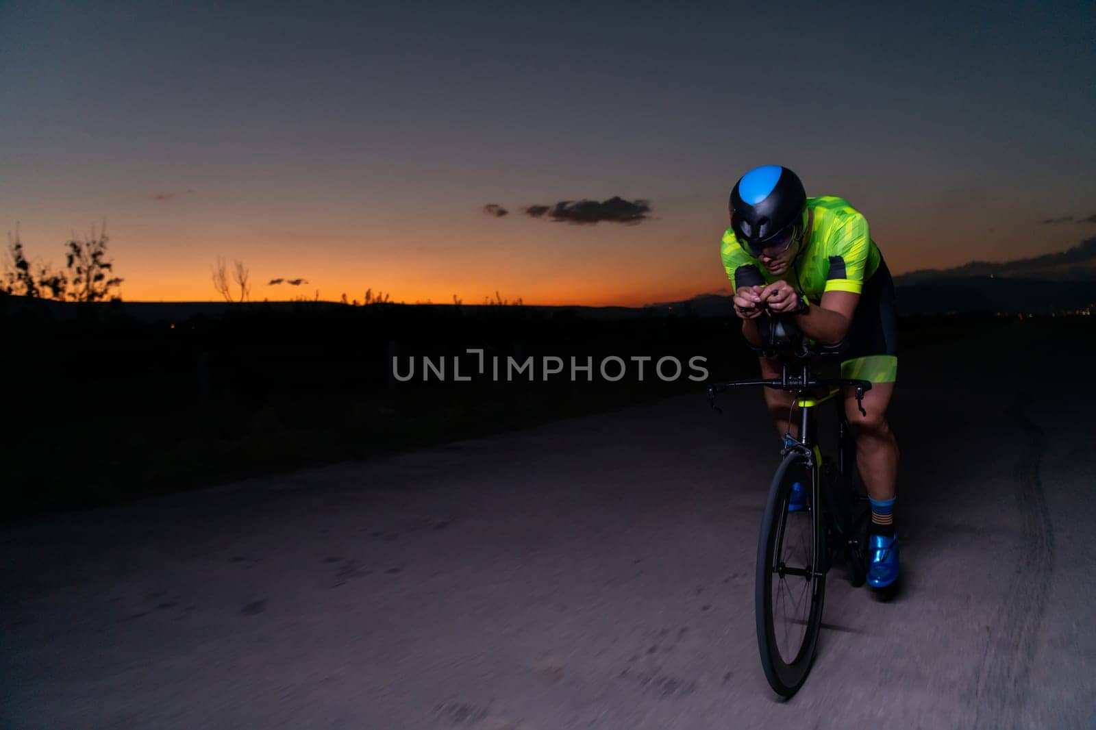 A triathlete rides his bike in the darkness of night, pushing himself to prepare for a marathon. The contrast between the darkness and the light of his bike creates a sense of drama and highlights the athlete's determination and perseverance