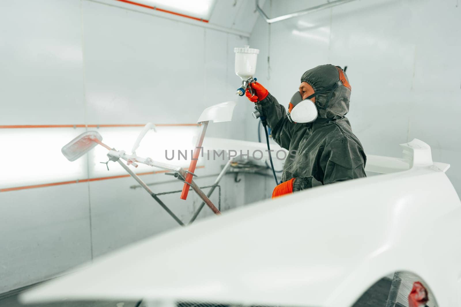 Auto painter painting a car with vaporizer gun inside a paint booth close up