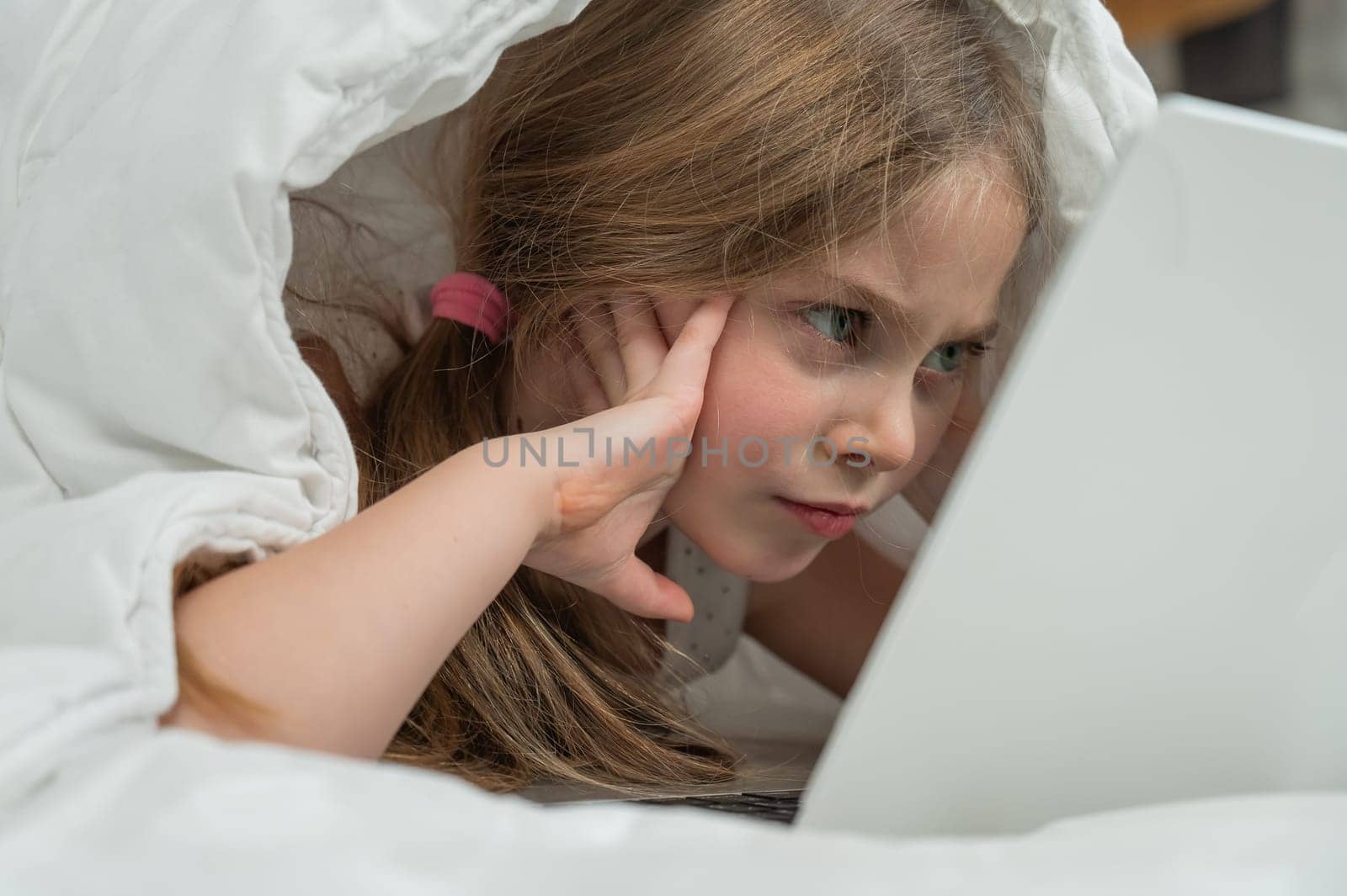 Portrait of a cute little girl using a laptop while lying under a blanket. by mrwed54