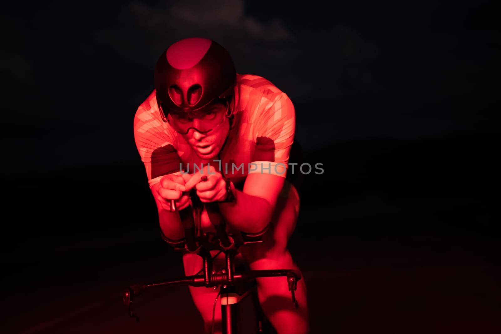 A triathlete rides his bike in the darkness of night, pushing himself to prepare for a marathon. The contrast between the darkness and the light of his bike creates a sense of drama and highlights the athlete's determination and perseverance