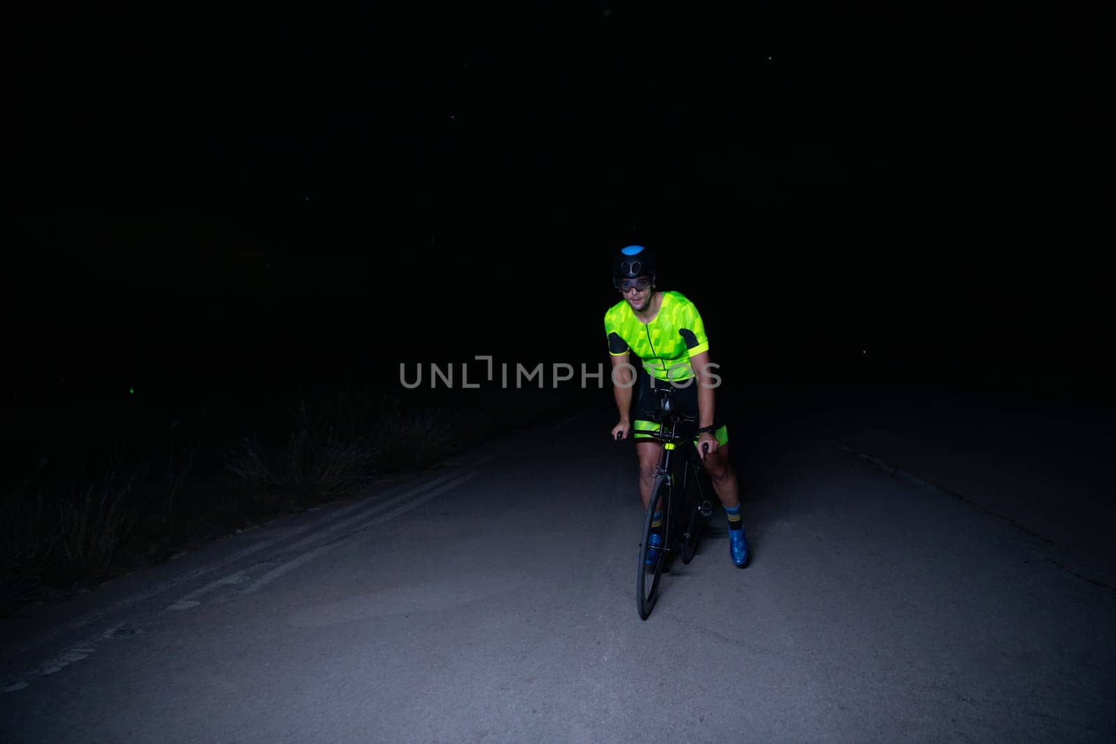 A triathlete rides his bike in the darkness of night, pushing himself to prepare for a marathon. The contrast between the darkness and the light of his bike creates a sense of drama and highlights the athlete's determination and perseverance. by dotshock