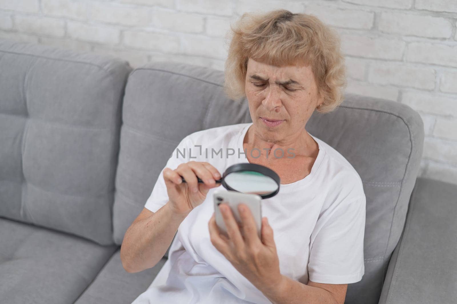 Elderly Caucasian woman with myopia and trying to read a message on a smartphone using a magnifying glass