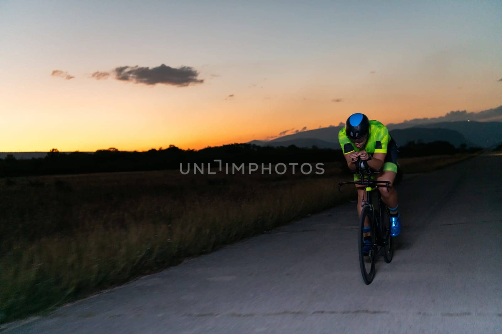 A triathlete rides his bike in the darkness of night, pushing himself to prepare for a marathon. The contrast between the darkness and the light of his bike creates a sense of drama and highlights the athlete's determination and perseverance. by dotshock